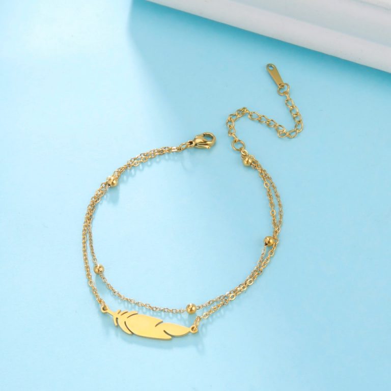 Un Bracelet Chaîne de Cheville Pied Plume Argent et Doré avec une plume.