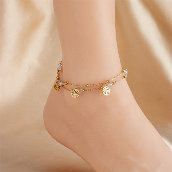 Un pied de femme orné d'un bracelet de cheville arbre de vie en acier inoxydable et de charms bijoux.