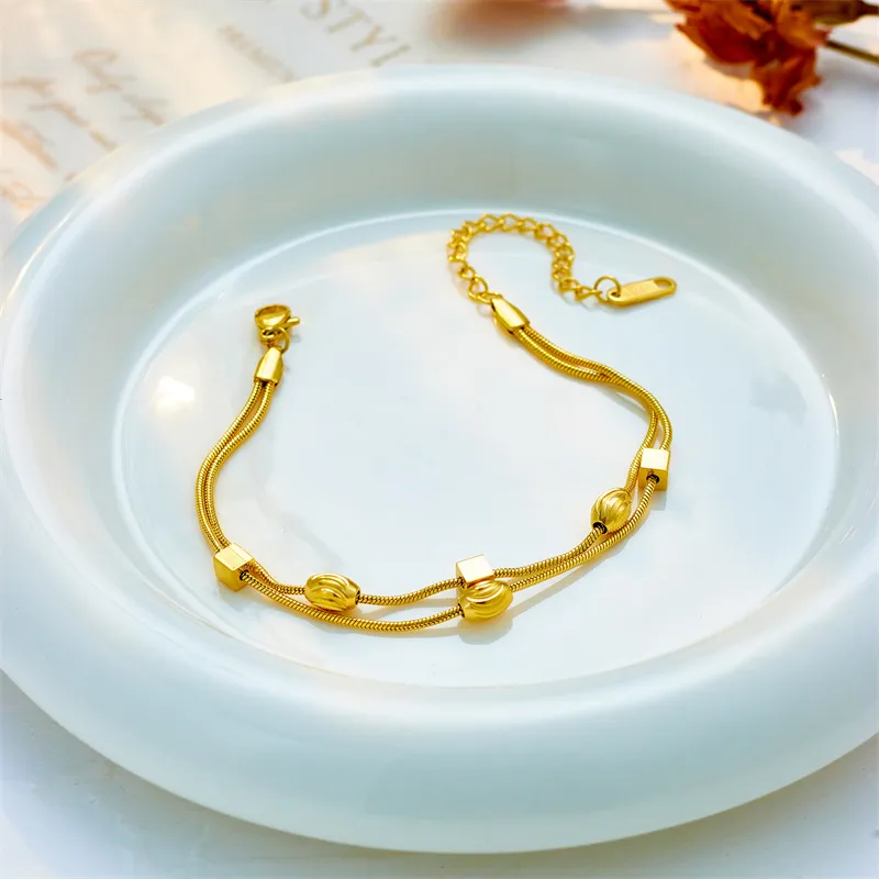 Un bracelet plaqué or en acier inoxydable pour femme à double breloque, posé élégamment sur une assiette.