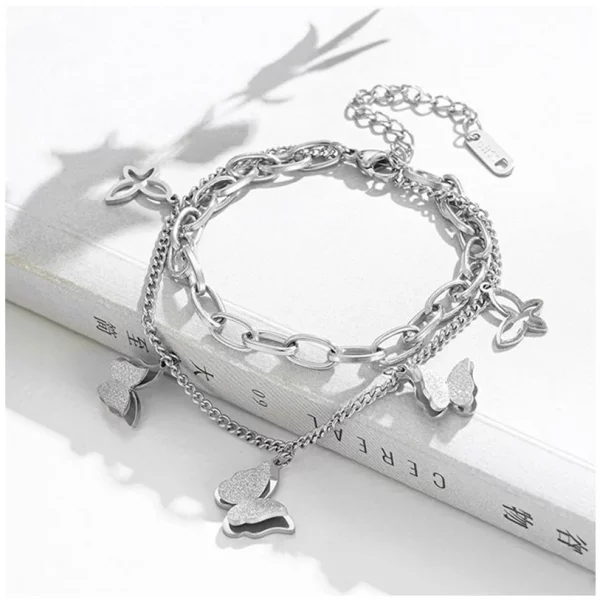 Un Bracelet en Acier Inoxydable Triple Pendentif Papillon en argent avec des breloques sur un livre.