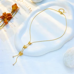 Un Collier Papillons Verticaux en Acier Inoxydable doré orne une assiette blanche parmi des fleurs délicates, mettant en valeur sa beauté.