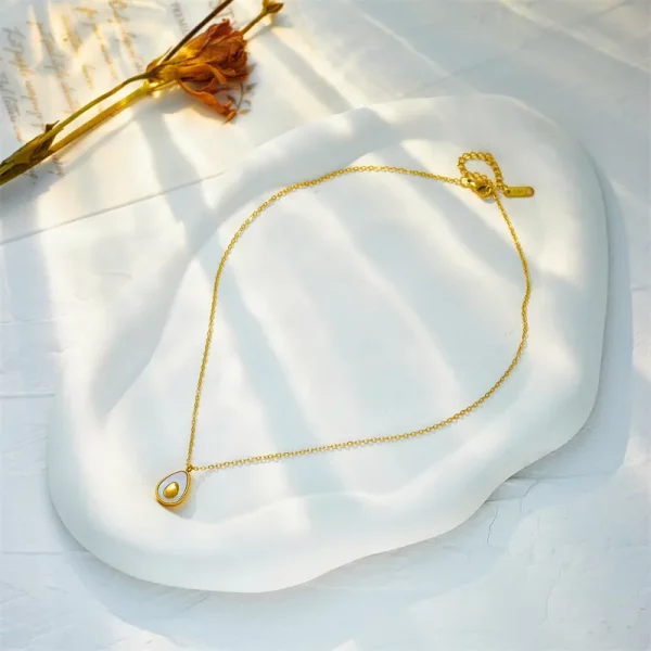 Un collier en acier inoxydable doré avocat avec une perle sur le dessus d'une assiette blanche.