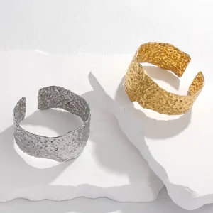 Deux bracelets jonc manchette en argent et or sur une surface blanche.
