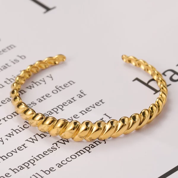 Un bracelet jonc torsadé en acier inoxydable plaqué or posé sur un livre.