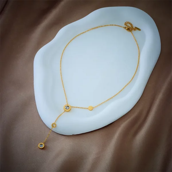 Un Collier acier inoxydable femme doré médaillon avec diamants sur plaque blanche.