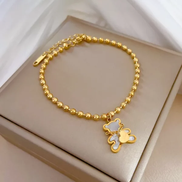 Un bracelet en acier inoxydable perlé plaqué or avec un pendentif ours blanc.