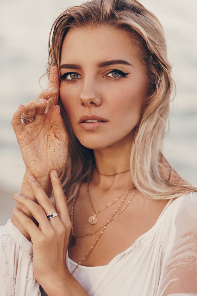 Une belle femme posant sur la plage avec sa main sur son visage, portant de superbes bijoux en acier inoxydable.