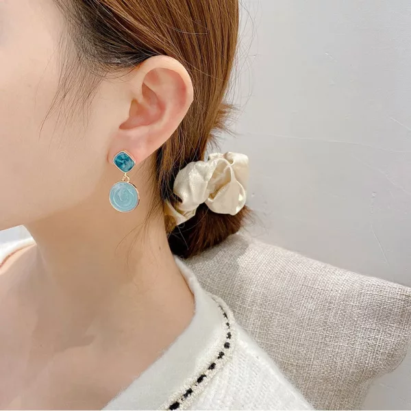 Une femme portant une paire de boucles d'oreilles Boucles d'Oreilles Asymétriques Carrées et Rondes avec une pierre bleue.