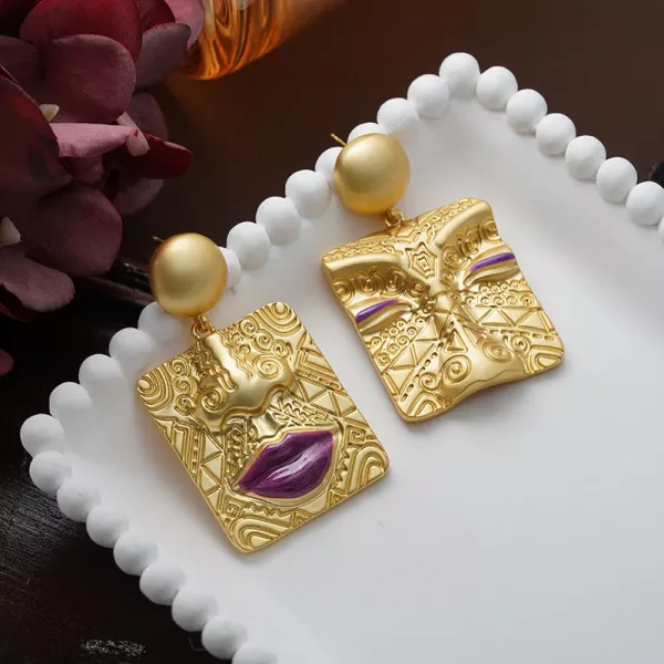Une paire de boucle d'oreille pendante asymétrique carrés dorés et violettes sur une assiette blanche.