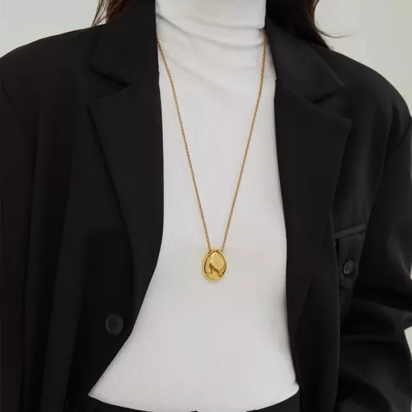 Une femme portant une veste noire et un collier doré comportant un collier cailloux ovale en acier inoxydable.
