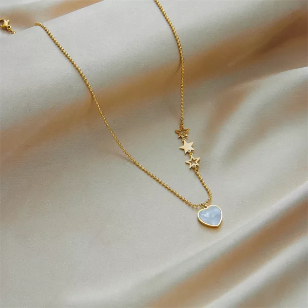 Un collier pendentif Cœur Blanc Chaîne Dorée avec des étoiles sur une chaîne.