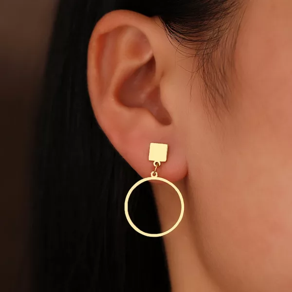 Une oreille de femme avec une boucle d'oreille pendante asymétrique géométrique.