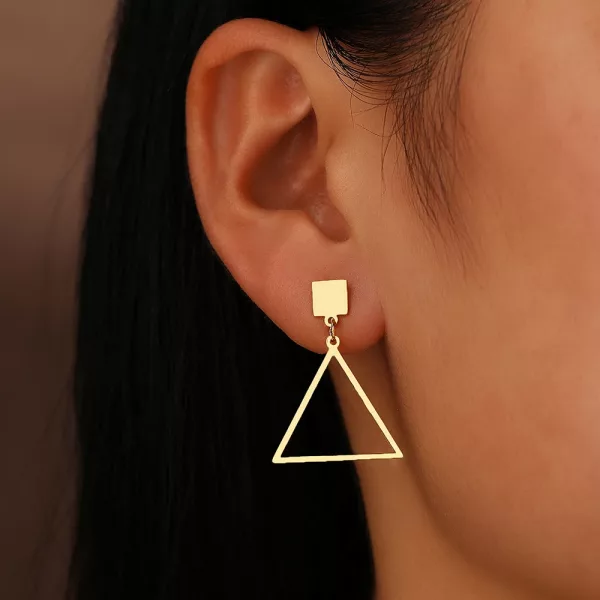Une femme portant une paire de boucle d'oreille pendante asymétrique géométrique en or.