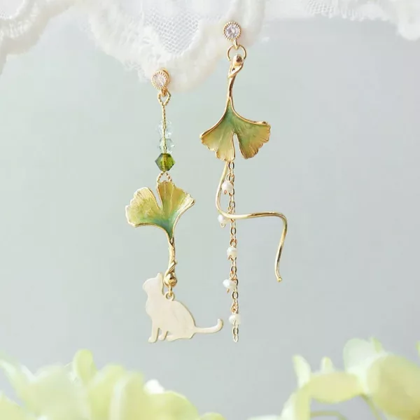 Une paire de Boucle d'Oreille Dépareillée tendance nature chat avec un chat et des feuilles de ginkgo.
