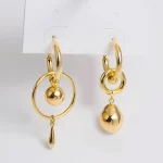 Une paire de boucles d'oreilles créoles en or dépareillées, l'une avec un cercle ouvert suspendu et de petites sphères, l'autre avec des créoles liées et une grande breloque en or en forme de larme. asymétrique