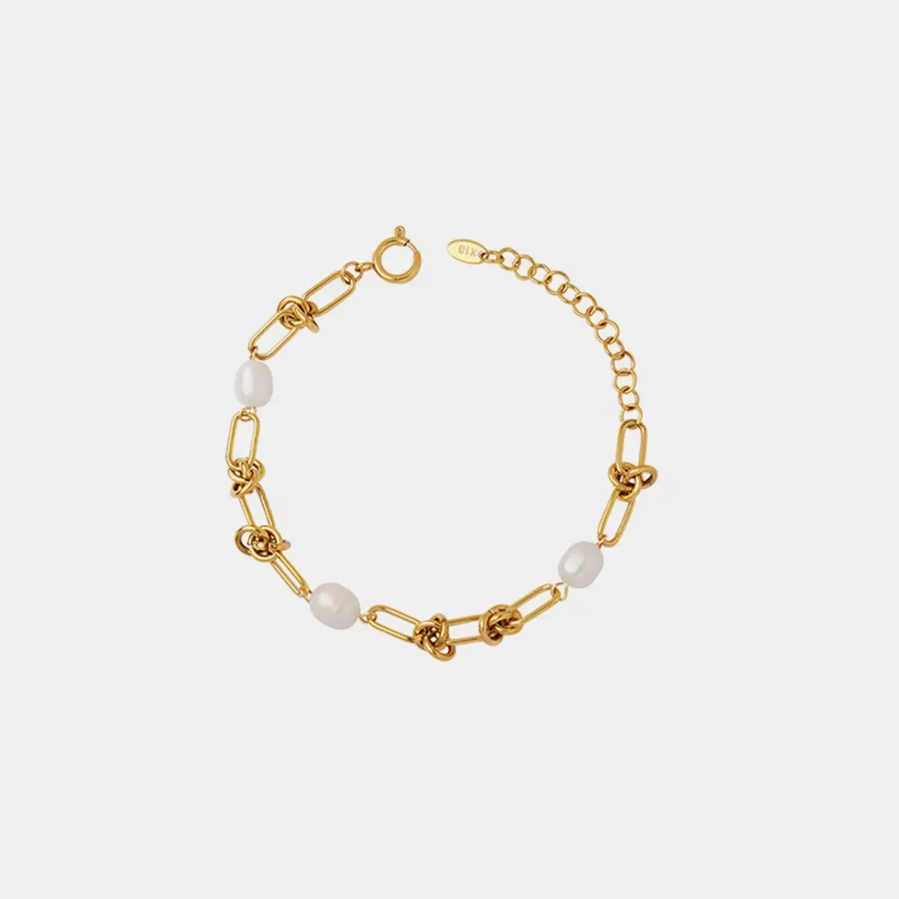 Bracelet en chaîne d'or avec des maillons entrelacés, des accents de perles et un fermoir ajustable sur un fond blanc uni.