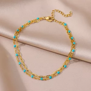 Bracelet en chaîne dorée avec des perles turquoises, avec un design à double couche et un fermoir réglable, présenté sur un tissu en satin beige.
