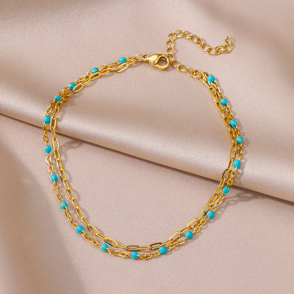 Bracelet en chaîne dorée avec des perles turquoises, avec un design à double couche et un fermoir réglable, présenté sur un tissu en satin beige.