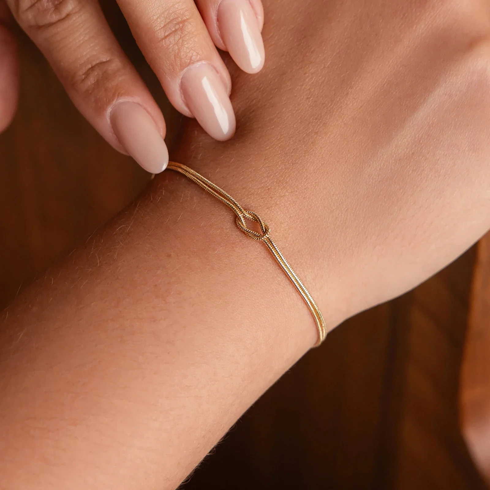 Une main aux ongles manucurés porte au poignet un délicat bracelet en or orné d'un petit nœud.