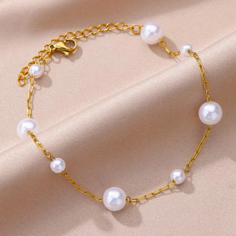 Un bracelet en chaîne d'or avec des perles blanches régulièrement espacées sur un fond de tissu beige.
