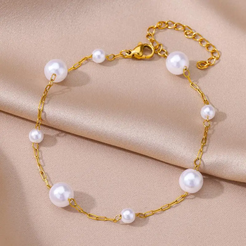 Un délicat bracelet en chaîne d'or avec des perles blanches espacées régulièrement et de tailles différentes, présentées sur un tissu de satin beige.