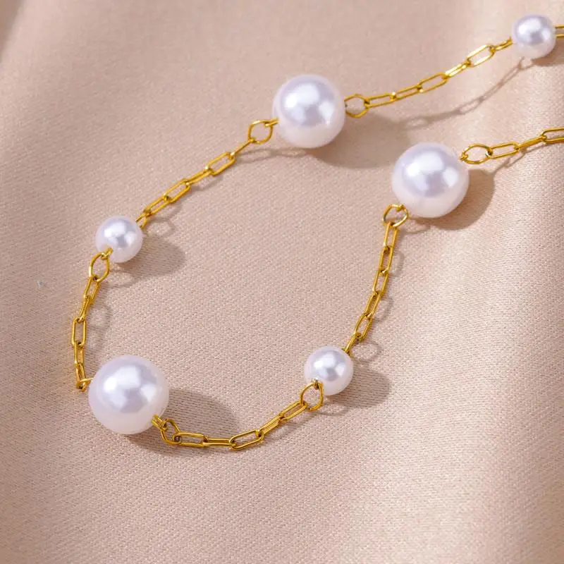 Un collier à chaîne en or avec des perles blanches est présenté sur un fond de tissu satiné beige clair.
