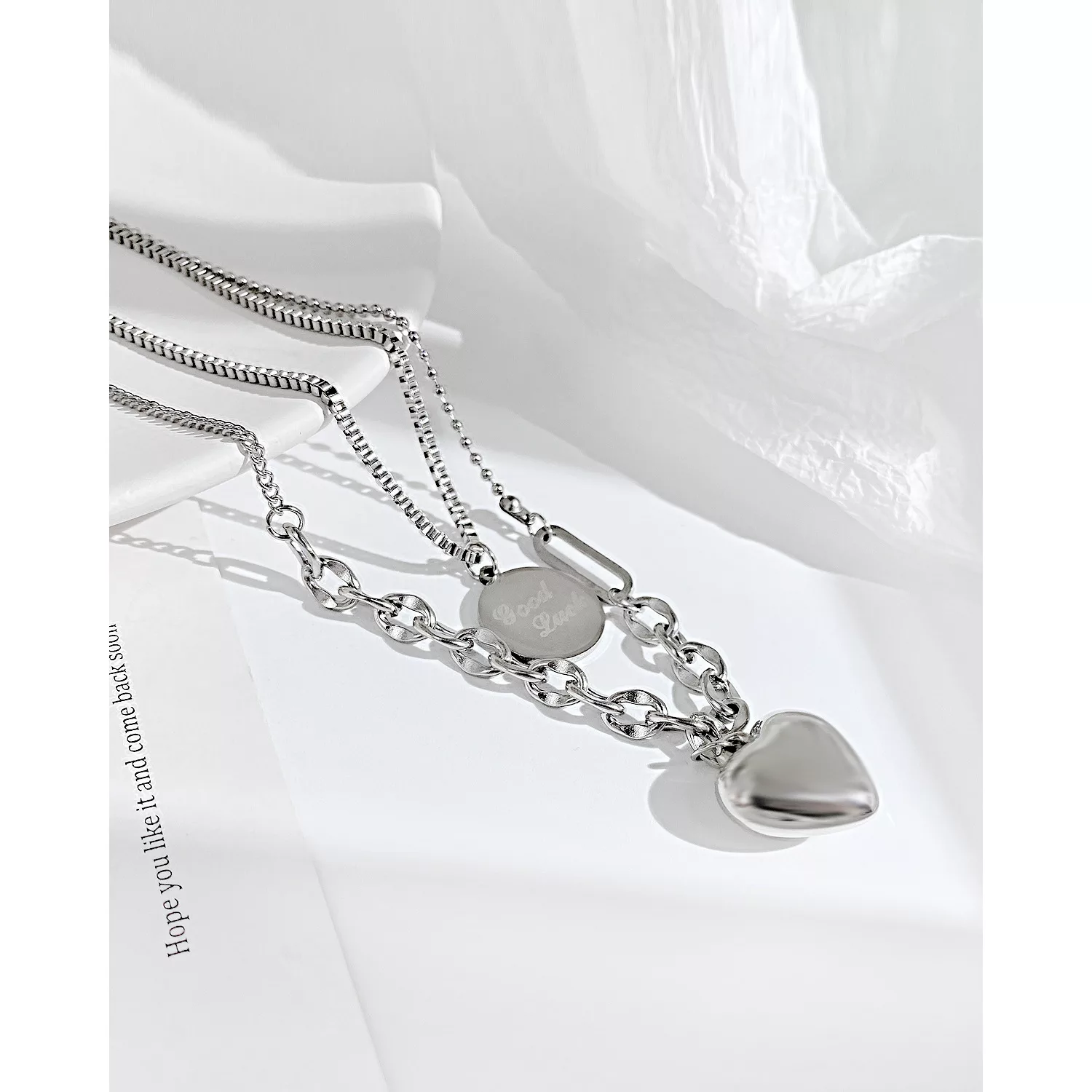 Collier en argent avec un pendentif en forme de cœur et une breloque ovale gravée sur une surface blanche.
