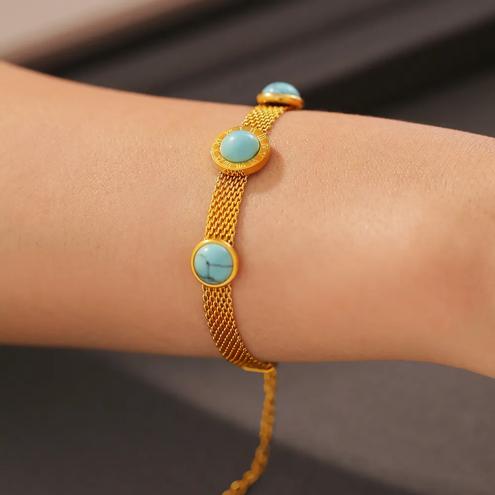 Un bracelet en maille d'or avec trois pierres turquoises rondes est porté au poignet d'une personne.