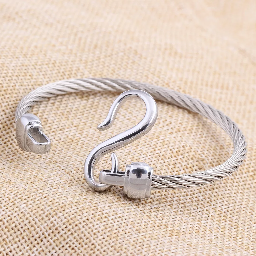 Un bracelet en fil métallique torsadé argenté avec un fermoir à boucle et crochet est présenté sur un fond de tissu beige texturé.