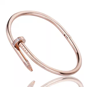 Bracelet forme clou en or rose conçu pour ressembler à un ongle plié, partiellement incrusté de petites pierres précieuses transparentes, présentées sur un fond blanc.
