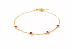 Le Bracelet chaîne dorée perlé avec pierres rouges - Ava présente cinq petites pierres rouges régulièrement espacées sur une délicate chaîne en or, sur fond blanc.