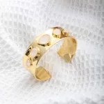 Un bracelet manchette en or, orné d'incrustations de pierres blanches ovales et rondes, est présenté sur un fond en tissu blanc texturé.
