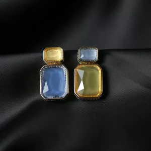 Une paire de boucles d'oreilles géométriques ornées de pierres rectangulaires bleues et jaunes serties dans du métal, présentées sur un fond de satin noir.