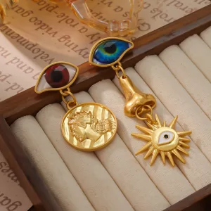 Deux boucles d'oreilles en or dépareillées sont exposées : l'une ornée d'un œil et d'une pièce de monnaie, l'autre d'un œil, d'un nez et d'un pendentif en forme de soleil avec un petit œil en son centre.