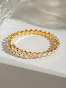 Un bracelet en or orné de deux rangées de pierres précieuses blanches rondes, présenté sur un fond clair aux ombres douces.