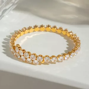 Un bracelet en or orné de deux rangées de pierres précieuses blanches rondes, présenté sur un fond clair aux ombres douces.