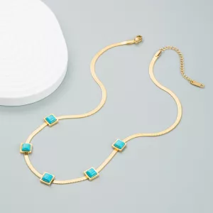 Collier à chaîne en or orné de cinq pierres de turquoise carrées espacées de manière régulière, présenté sur un fond gris clair à côté d'un objet blanc texturé.
