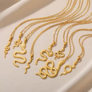 Cinq pendentifs en or en forme de serpent, suspendus à des chaînes en or, sont disposés en rangée sur un fond de tissu beige clair.