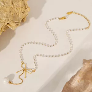 Un collier composé d'une chaîne en or, de petites perles blanches, d'un pendentif en forme de nœud en or et d'une seule grosse perle, présenté sur un fond clair rehaussé de touches de pierre.